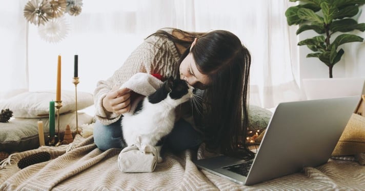 women kissing cat on bed with laptop out