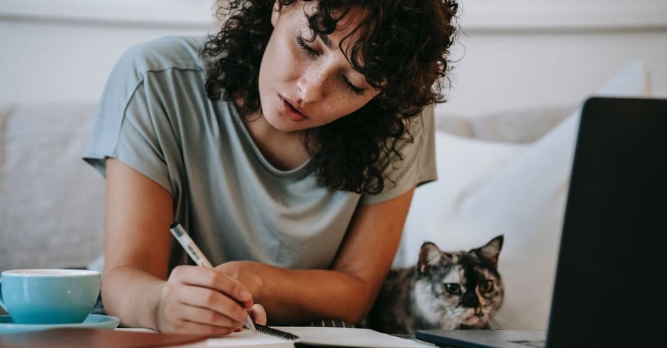 Women writing in key pet insurance terms in notebook with cat lying next to her